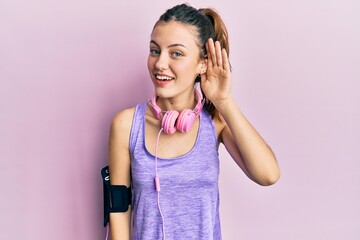 Young brunette woman wearing sportswear and headphones smiling with hand over ear listening and hearing to rumor or gossip. deafness concept.