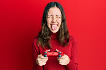 Young brunette woman playing video game holding controller sticking tongue out happy with funny expression. © Krakenimages.com