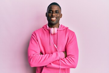 Young african american man wearing gym clothes and using headphones happy face smiling with crossed arms looking at the camera. positive person.