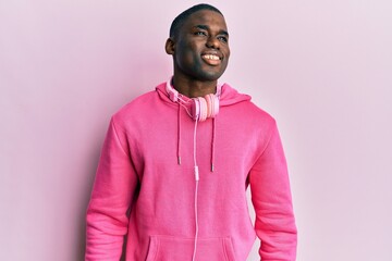 Obraz premium Young african american man wearing gym clothes and using headphones looking away to side with smile on face, natural expression. laughing confident.