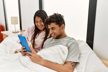 Fototapeta premium Young latin couple smiling happy using touchpad lying on the bed at bedroom.