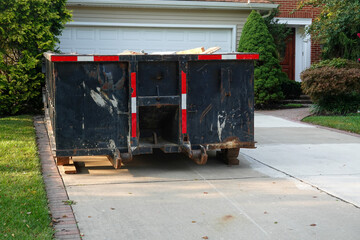 Long blue dumpster full of wood and other debris in the driveway in front of a house in the suburbs...