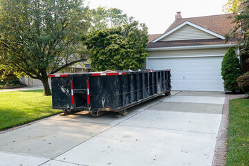 Long blue dumpster full of wood and other debris in the driveway in front of a house in the suburbs...
