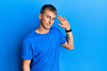 Naklejka premium Young caucasian man wearing casual blue t shirt waiving saying hello happy and smiling, friendly welcome gesture