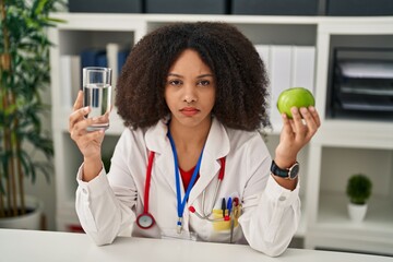 Young african american dietitian woman holding fresh apple and water depressed and worry for...
