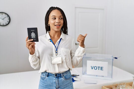 Young african american woman at political campaign election holding canada passport pointing thumb up to the side smiling happy with open mouth