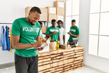 Group of young african american volunteers working at charity center. Man smiling happy writing on...