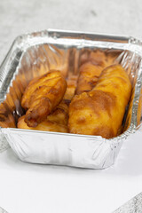 Battered chicken portions in a foil takeaway tray with lid. On a concrete background