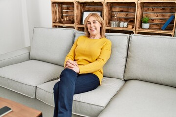 Middle age blonde woman smiling happy relaxed sitting on the sofa at home.