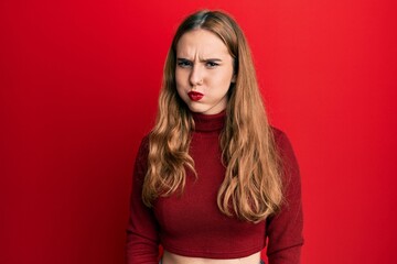 Young blonde woman wearing turtleneck sweater puffing cheeks with funny face. mouth inflated with air, crazy expression.