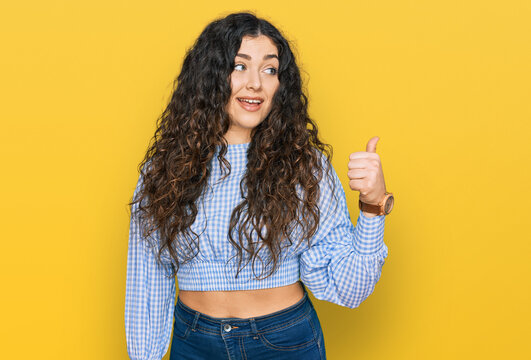 Young hispanic girl wearing casual clothes smiling with happy face looking and pointing to the side with thumb up.