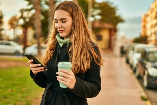 Young blonde girl using smartphone drinking coffee at the city.