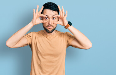 Fototapeta premium Hispanic man with beard wearing casual t shirt trying to open eyes with fingers, sleepy and tired for morning fatigue