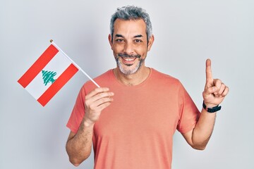 Handsome middle age man with grey hair holding lebanon flag smiling with an idea or question pointing finger with happy face, number one