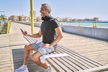 Middle age hispanic man wearing sportswear using smartphone at seaside