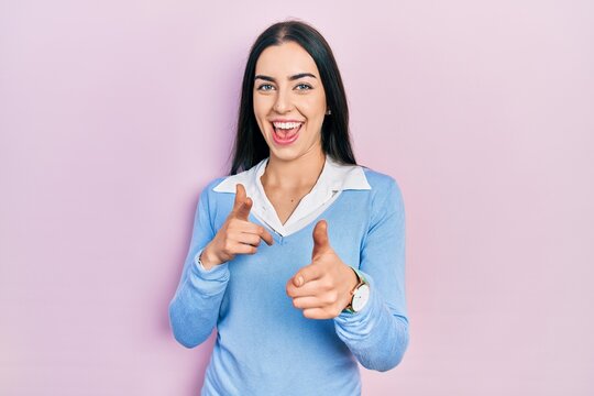 Beautiful woman with blue eyes standing over pink background pointing fingers to camera with happy and funny face. good energy and vibes.