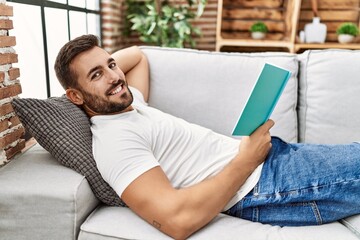 Young hispanic man smiling confident reading book at home