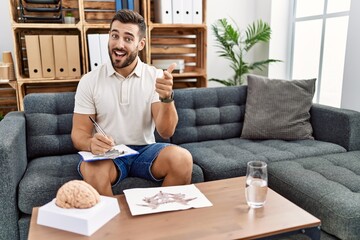 Handsome hispanic man working with rorschach test at psychology clinic pointing fingers to camera...