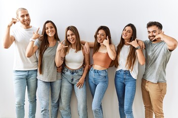 Obraz premium Group of young friends standing together over isolated background smiling doing phone gesture with hand and fingers like talking on the telephone. communicating concepts.