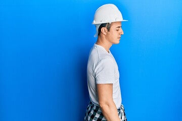 Handsome young man wearing builder uniform and hardhat looking to side, relax profile pose with natural face with confident smile.