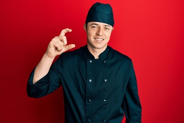 Handsome young man wearing professional cook uniform and hat smiling and confident gesturing with...
