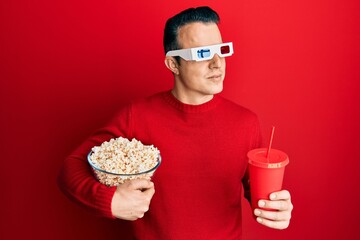 Handsome young man eating popcorn and soda wearing 3d glasses smiling looking to the side and staring away thinking.