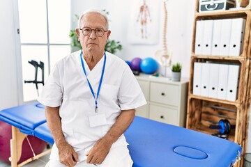 Obraz premium Senior physiotherapy man working at pain recovery clinic relaxed with serious expression on face. simple and natural looking at the camera.