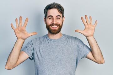 Fototapeta premium Caucasian man with beard wearing casual grey t shirt showing and pointing up with fingers number ten while smiling confident and happy.