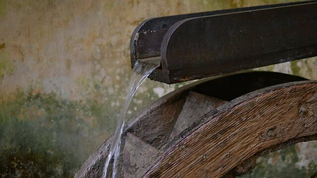 Close up view of old waterwheel mill. Water wheel in rural area. Water falls on an old water wheel with concrete house in the background. The old wooden mill wheel. Static shot, real time