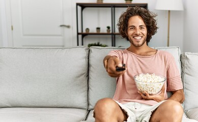 Young hispanic man watching movie sitting on the sofa at home.