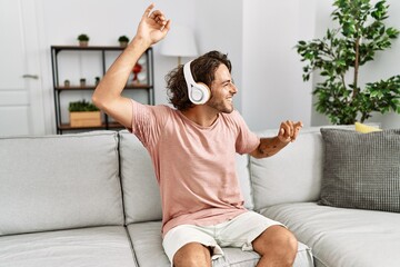Young hispanic man listening to music and dancing sitting on the sofa at home.