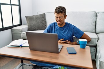 Young handsome hispanic man using laptop sitting on the floor with hand on stomach because nausea, painful disease feeling unwell. ache concept.