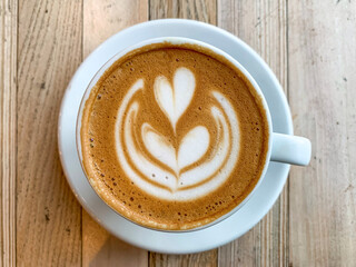 A cup of coffee latte On a wooden table. A mug of flat white coffee on a wooden background. Coffee art. Heart flower shape latte art