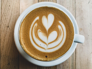 A cup of coffee latte On a wooden table. A mug of flat white coffee on a wooden background. Coffee art. Heart flower shape latte art