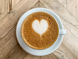 A mug of flat white or latte art coffee on a wooden background. Coffee art. Heart flower shape latte art