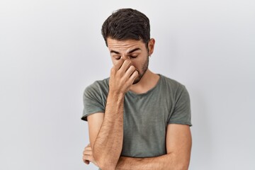 Young hispanic man with beard wearing casual t shirt over white background tired rubbing nose and eyes feeling fatigue and headache. stress and frustration concept.