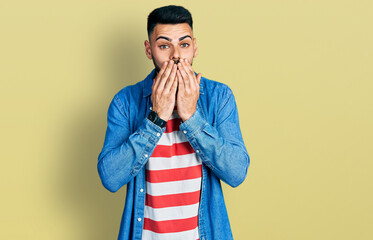 Young hispanic man with beard wearing casual denim jacket laughing and embarrassed giggle covering...
