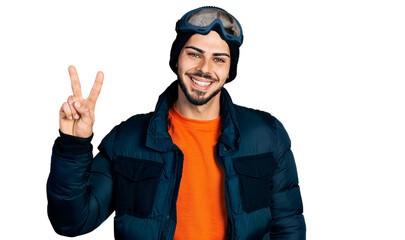 Young hispanic man with beard wearing snow wear and sky glasses showing and pointing up with fingers number two while smiling confident and happy.