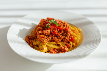 White plate with bolognese pasta and parsley leaf on the top standing on table. Preparing traditional italian meal from noodles.