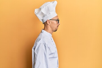 Bald man with beard wearing professional cook uniform looking to side, relax profile pose with...