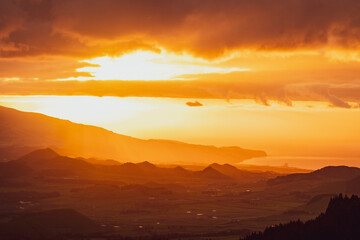 Sunrise over landscape with mountains, orange light, sun rising.
