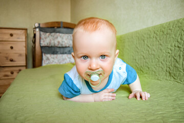 The baby crawls on the sofa with a pacifier in the home interior. Close-up.