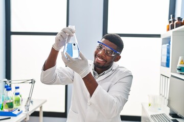 Young african american man wearing scientist uniform holding test tube at laboratory