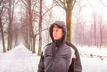 A man walks through a snowy park in winter. Portrait, close-up. Pink colors.