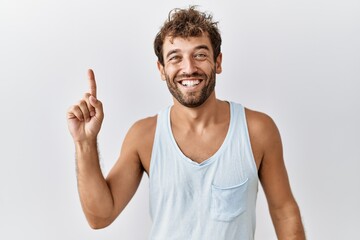 Young handsome man standing over isolated background pointing finger up with successful idea. exited and happy. number one.