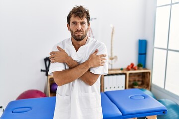 Young handsome physiotherapist man working at pain recovery clinic shaking and freezing for winter cold with sad and shock expression on face