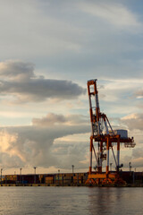 A container crane stands bathed in the orange evening sun at the Kushiro Port quay at dusk.