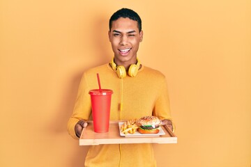 Young african american guy eating a tasty classic burger winking looking at the camera with sexy...