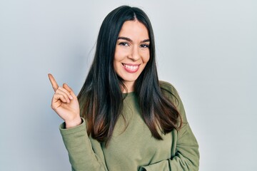 Young brunette woman wearing casual green sweater smiling happy pointing with hand and finger to the side