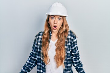 Young caucasian woman wearing architect hardhat scared and amazed with open mouth for surprise, disbelief face